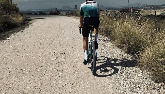 Bicicleta de perfil en ruta exterior con paisaje de cinturón montañoso y cielo nublado.