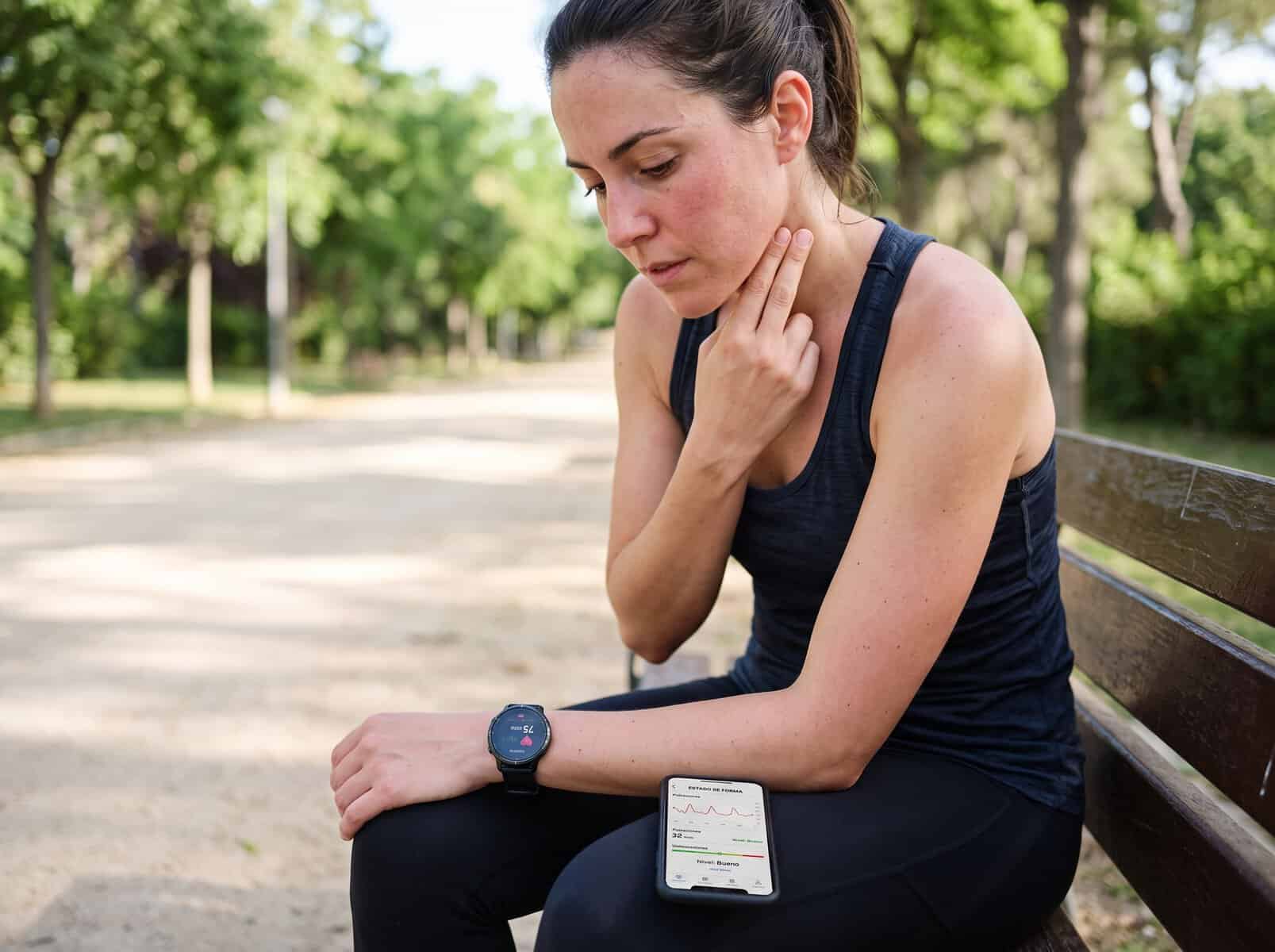 Ciclista tomándose el pulso manualmente en el cuello, con reloj y móvil mostrando el estado de forma